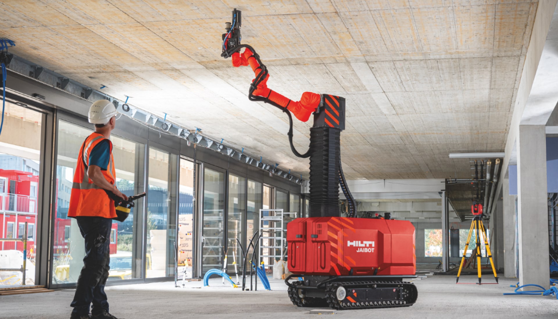 Rakennustyöntekijä käyttää turvallisesti Jaibot-robottia sisäkattojen poraukseen työmaalla