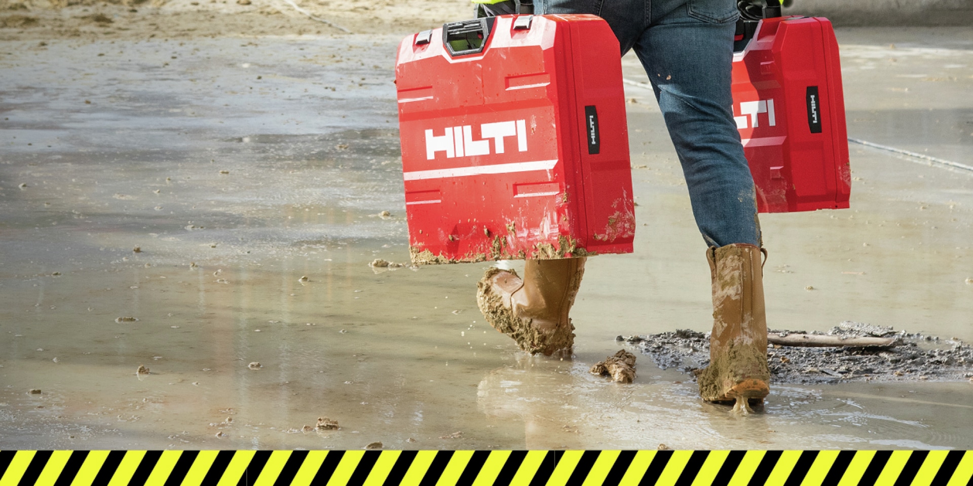 Rakennustyöntekijä työmaalla pitelemässä Hilti-työkalusalkkuja